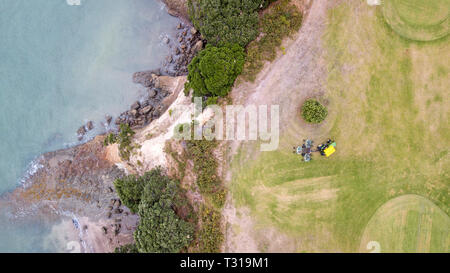 Vista aerea di un trattore Falciare il prato in uno dei campi da golf vicino alla spiaggia nel punto di musica, Auckland, Nuova Zelanda Foto Stock