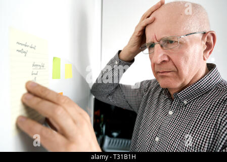 Confuso uomo anziano con demenza guardando le note sul frigorifero Foto Stock