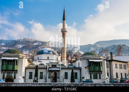 Un minareto sorge su edifici attraverso il fiume dalla città vecchia di Sarajevo. Gazi Husrev-bey moschea. La Bosnia Erzegovina Foto Stock