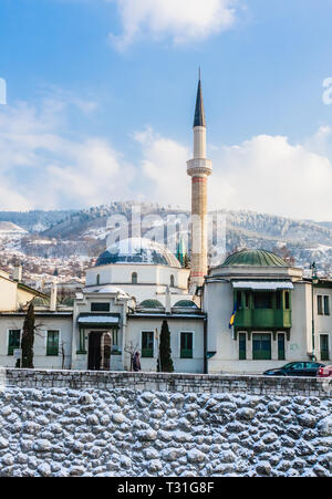 Un minareto sorge su edifici attraverso il fiume dalla città vecchia di Sarajevo. Gazi Husrev-bey moschea. La Bosnia Erzegovina Foto Stock