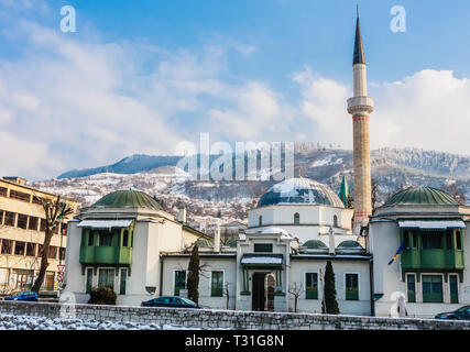 Un minareto sorge su edifici attraverso il fiume dalla città vecchia di Sarajevo. Gazi Husrev-bey moschea. La Bosnia Erzegovina Foto Stock