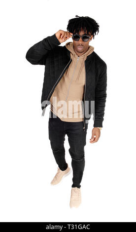 Un giovane bello African American man standing in studio in un abbigliamento informale e un paio di occhiali da sole, isolato per sfondo bianco Foto Stock