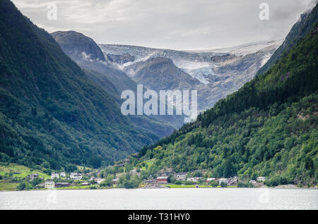 Vista in lontananza un ghiacciaio Buarbreen valley con un piccolo villaggio nella parte anteriore in Odda regione, Norvegia. Foto Stock