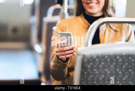 Donna sorridente che usa lo smartphone in treno, metropolitana, autobus o tram. Lady inviare messaggi con i mezzi pubblici o utilizzando la connessione wi-fi gratuita. Foto Stock