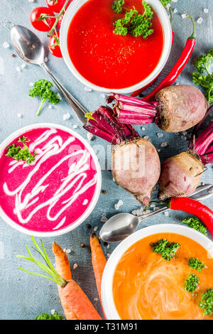 Set di varie crema di verdure zuppe, carote, barbabietole, Radice di pomodoro piccante purea di zuppe con fresche verdure organiche, blu sullo sfondo di calcestruzzo, spazio di copia Foto Stock