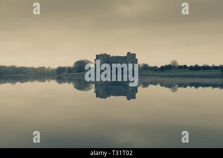 Carew Castle riflettendo in acqua in una nebbiosa mattina, Pembrokeshire in tonalità seppia Foto Stock