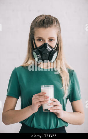 Donna bionda in maschera respiratoria tenendo un bicchiere di latte Foto Stock