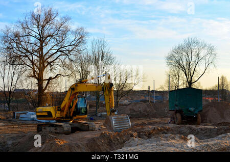 Escavatore cingolato con una benna nel terreno in corrispondenza di un sito di costruzione contro un cielo blu e al tramonto Foto Stock