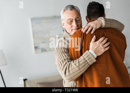 Senior uomo in bicchieri sorridere mentre abbracciando il figlio Foto Stock