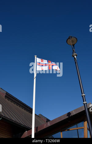 Bandiera RNLI fying da pennone e strada lampada a Craig y don scialuppa di salvataggio station contro un cielo blu con nuvole non in Llandudno North Wales UK Foto Stock