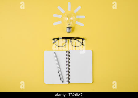 Appartamento laico, vista dall'alto, copia dello spazio. Tabella di pianificazione finanziaria al top con penna, notepad, occhiali e lampadina della luce su sfondo giallo. Concetto il brainstorming Foto Stock