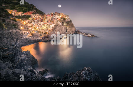 Un waxing gibbous luna sorge sopra la città di Manarola, che fa parte delle Cinque Terre in Liguria sulla costa d'Italia. Foto Stock