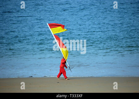 Giovane donna Life Guard a piedi che porta bandiera di avvertimento sulla Greve De Lecq Beach sull'isola di Jersey, nelle Isole del Canale, UK. Foto Stock