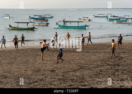 BADUNG,BALI/INDONESIA-aprile 02 2019: Asian adolescente di giocare a calcio o di calcio a Kuta beach con il tramonto o golden ore sfondo. Alcune tradizionali boa Foto Stock