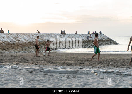 BADUNG,BALI/INDONESIA-aprile 02 2019: Asian adolescente di giocare a calcio o di calcio a Kuta beach con il tramonto o golden ore sfondo.Il cielo è nuvoloso e Foto Stock