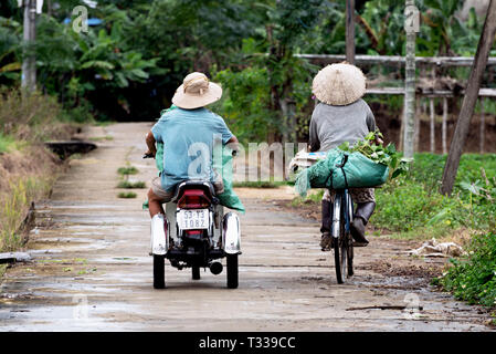 Strada di campagna, i lavoratori del trasporto dei prodotti agricoli da scooter e biciclette in Duy Xuyen, Vietnam Foto Stock