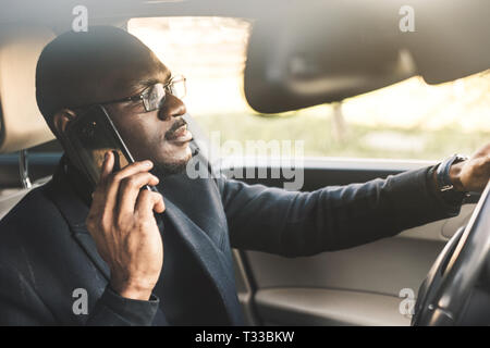 Un imprenditore alla guida di una costosa macchina possiede un telefono cellulare nella sua mano. Vita frettolosa Foto Stock