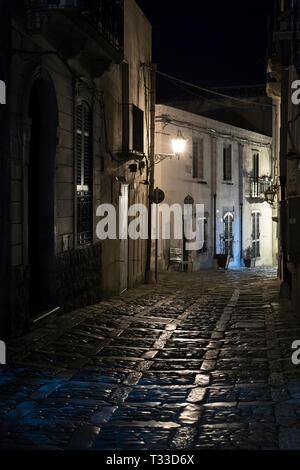 Lampade che brilla sulla pavimentazione di pietra di notte in strada di ciottoli vicolo di Erice, in Sicilia, Italia Foto Stock