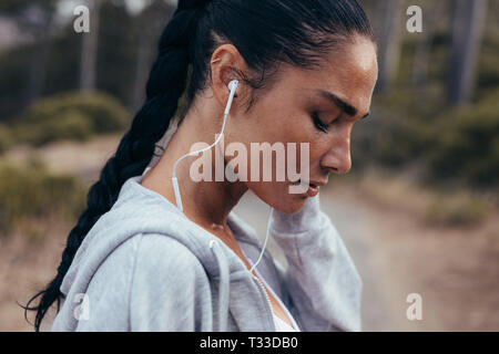 Vista laterale di un atleta femminile di indossare le cuffie per ascoltare musica. Sportive ascoltare musica all'aperto in mattina. Foto Stock