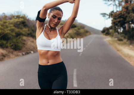 Sportivo da donna stretching le braccia mentre si cammina su una strada vuota nella mattina. Femmina rilassante runner i suoi muscoli mentre si lavora fuori all'aperto. Foto Stock