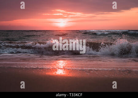 La riflessione della luce solare in acqua e sabbia sulla spiaggia. arancione tramonto mistico del mare del Giappone. Marea all'alba, le onde battere la schiuma del mare sulla sabbia sul Foto Stock