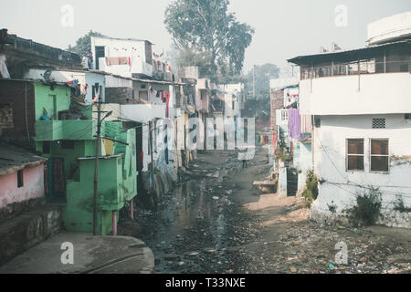 Un puzzolente flusso di liquame in baraccopoli. Area povera di Haridwar, India. Casa di poveri sulla collina di fronte un fiume sporco. problemi sociali della nostra Foto Stock