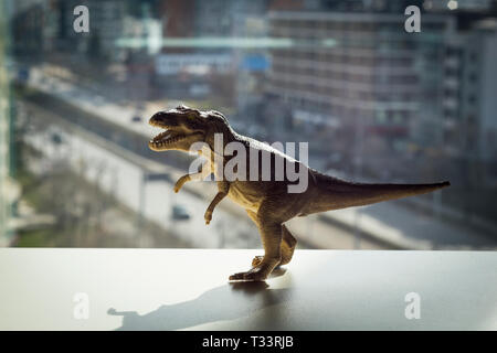 T-Rex dinosauro giocattolo con una città sfocata dietro Foto Stock