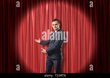 Giovane Imprenditore illuminato dai riflettori facendo un gesto presentando contro rosso teatro tenda. Foto Stock