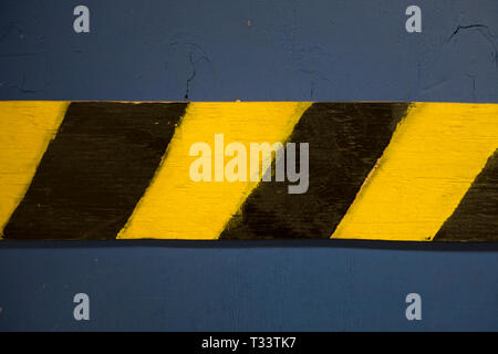 Nero verniciato giallo angolato di costruzione attenzione configurato linee su un legno bianco con sfondo blu scuro muro Foto Stock