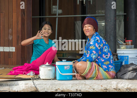 una giovane ragazza e sua madre in thailandia lavorando a fianco della strada preparando il cibo e ondeggiante con felice sorriso volti. Foto Stock