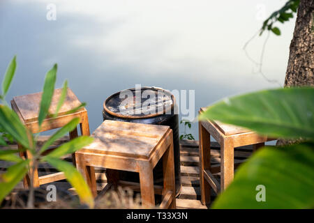 Vintage Sgabelli in legno sul balcone di legno sotto agli alberi, di fronte fiume di luce e di ombra Foto Stock