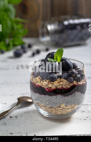 Dessert leggero di chia pudding con mirtillo, avena e marmellata fresca, servita in vetro sottile. Foto Stock