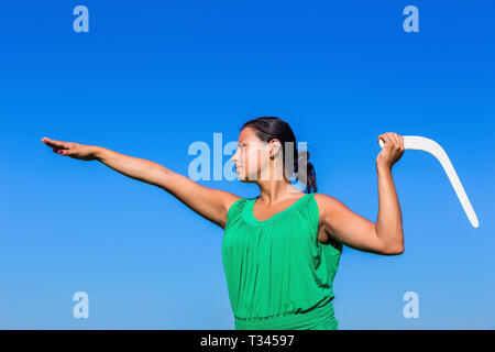 Giovane donna colombiano gettando boomerang bianco in aria blu Foto Stock