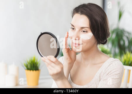 Ritratto di giovane e bella donna con trucco naturale applicare bianco sotto gli occhi le patch maschera di bellezza sul viso. Occhio di trattamento della pelle. Ritratto di donna con ey Foto Stock