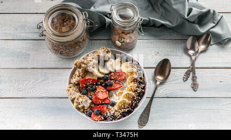 Banner di cibo. Una sana prima colazione in una ciotola: Cottage cheese, granola, banane, fragole, mirtilli e riso soffiato. Tavolo in legno sfondo Foto Stock