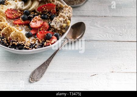 Close up sana colazione ciotola e cucchiaio: Cottage cheese, granola, banane, fragole, mirtilli e riso soffiato. Tavolo in legno sfondo Foto Stock