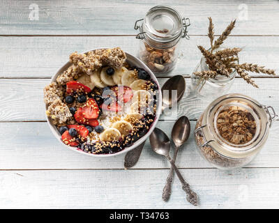 Concetto sana prima colazione. Cottage cheese, granola, banane, fragole, mirtilli e riso soffiato. Tavolo in legno sfondo. Vista superiore Foto Stock