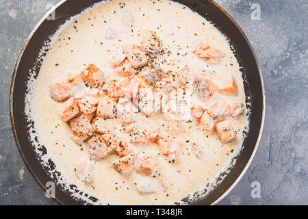 A cubetti di salmone sono fritte in crema di latte in una padella. Vista dall'alto. Foto Stock