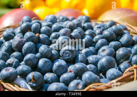 Fresche biologiche mature i mirtilli in un cestello con altri sfocati fuori fuoco frutta e verdura sullo sfondo, in un mercato vicino fino Foto Stock