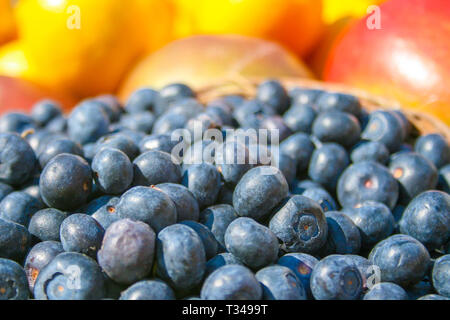 Fresche biologiche mature i mirtilli in un cestello con altri sfocati fuori fuoco frutta e verdura sullo sfondo, in un mercato vicino fino Foto Stock