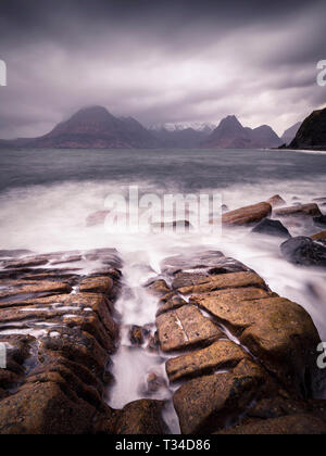 Mare che fluisce in un canale nella roccia come onde venire in e out che conduce al nero Cullin montagne attraverso la baia. Foto Stock