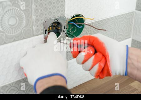 Ristrutturazione e costruzione in cucina, close-up di elettricisti lato uscita di installazione su parete con piastrelle in ceramica utilizzando strumenti professionali. Foto Stock