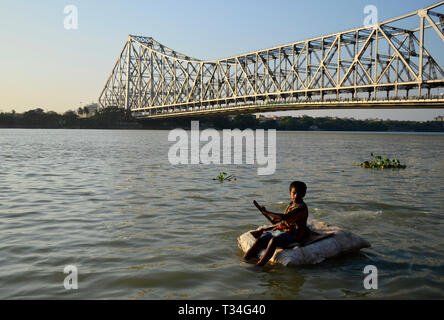 Un ragazzo galleggia su un sacco di thermocol sul fiume Ganga in Kolkata, India