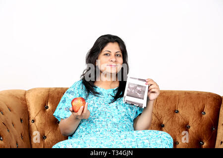 Immagine della donna in stato di gravidanza è tenuta ad ultrasuoni del bambino e Apple in mano. Isolato su uno sfondo bianco. Foto Stock