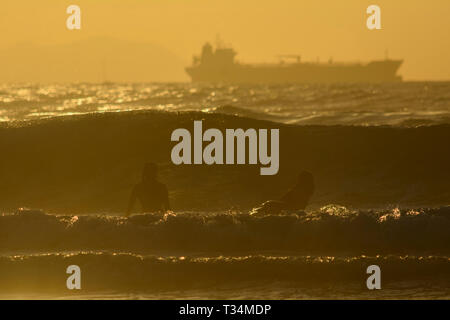 Due surfisti in attesa di prendere un'onda al tramonto, spiaggia di Sopelana, Biscaglia, Paesi Baschi Foto Stock