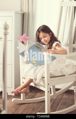Ragazza seduta in una sedia a dondolo la lettura di un libro Foto Stock