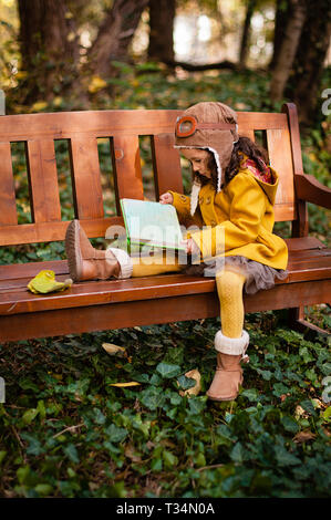 Ragazza che indossa un aviatore cappello e occhiali seduta su una panchina a leggere un libro, Bulgaria Foto Stock
