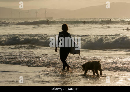 Silhouette di un surfista femmina passeggiando per il surf con il suo cane, Bilbao, Spagna Foto Stock