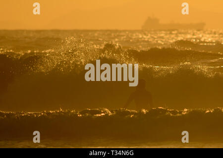 Silhouette di un surfista cattura un'onda al tramonto, spiaggia di Sopelana, Biscaglia, Spagna Foto Stock