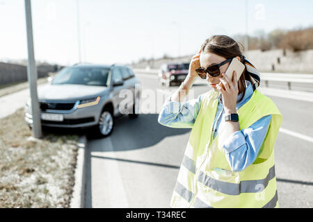 In imbarazzo donna che chiama assistenza stradale in piedi vicino alla macchina durante l'incidente stradale in autostrada Foto Stock